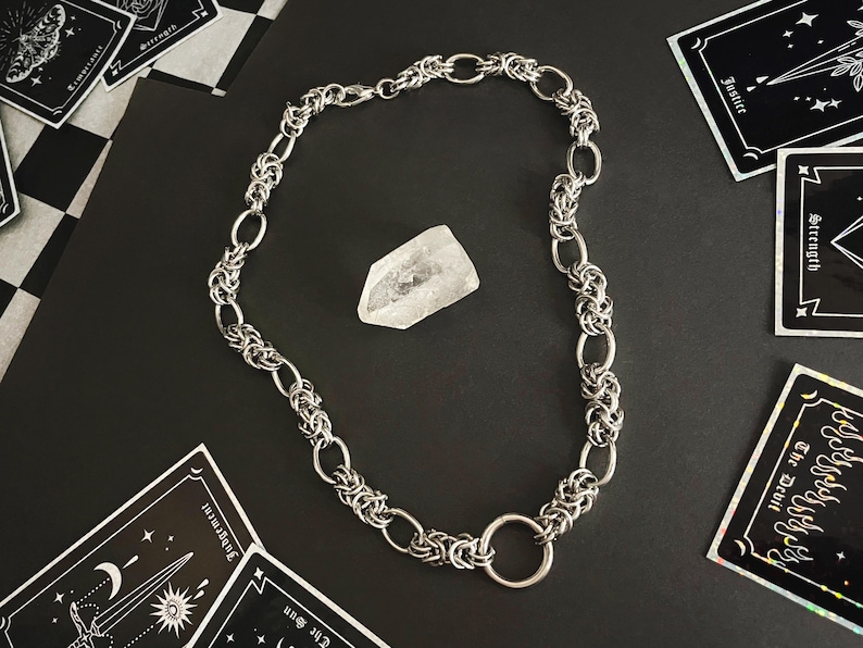 K&ouml;nnte beinhalten: Eine silberne Kettenkette mit einem gro&szlig;en, runden, silbernen Ringverschluss. Die Kette besteht aus ineinandergreifenden Metallgliedern.
