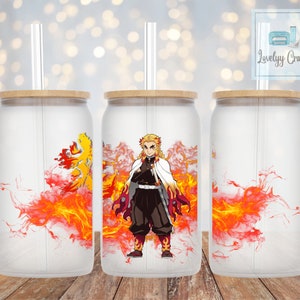 Op de afbeelding: Drie glazen bekers met bamboe deksels en doorzichtige rietjes. Elke beker heeft een ontwerp van een personage uit de anime-serie "Demon Slayer", met een vurige achtergrond. De bekers zijn mat en staan op een houten oppervlak.