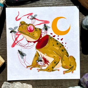 May include: A surreal illustration of a frog with a crescent moon in the background. The frog is depicted with a gaping mouth and its insides are visible, with flies and red string-like tendrils coming out of its body.