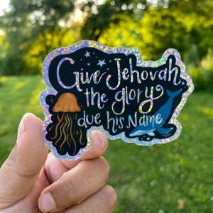 Op de afbeelding: Een holografische sticker met de tekst "Give Jehovah the glory due his Name". De sticker bevat illustraties van een kwal en een walvis. De tekst en illustraties zijn in tinten blauw, oranje en zwart.