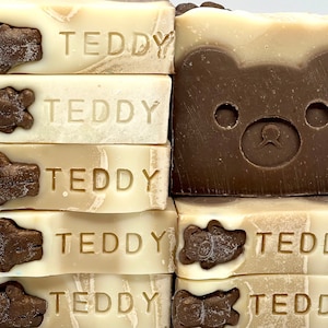 May include: Stack of five brown and white soap bars with a teddy bear design and the word "TEDDY" embossed on each bar.