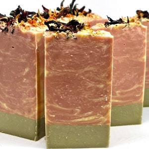 May include: Four bars of handmade soap with a pink and white swirl design. The soap is topped with dried flowers and herbs.