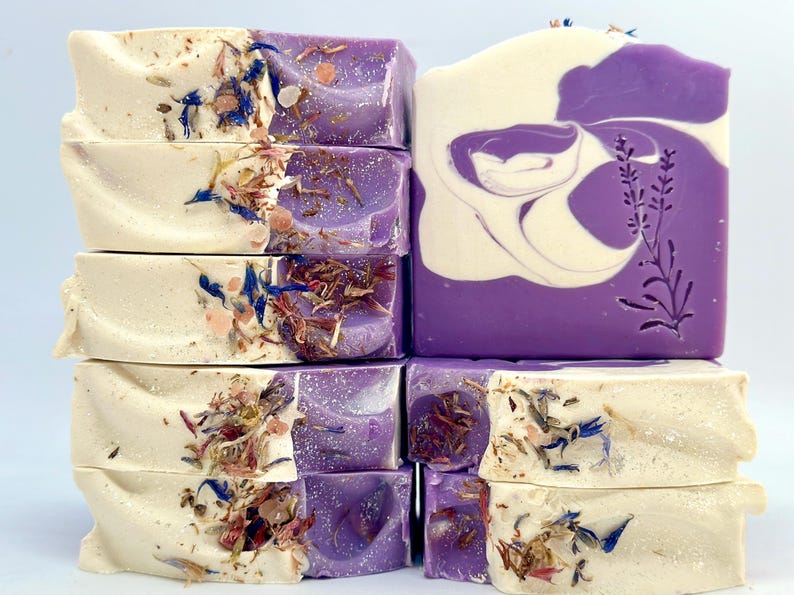 K&ouml;nnte beinhalten: Ein Stapel handgemachter Seifenst&uuml;cke mit Lavendel-Duft. Die Seifen sind eine Mischung aus Wei&szlig; und Lila mit getrockneten Blumen und Kr&auml;utern, die in die Seife eingebettet sind.