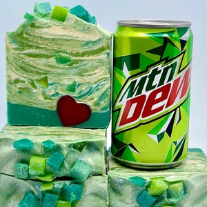 May include: Four bars of green and white soap with a red heart design. The soap is stacked on top of a can of Mountain Dew.