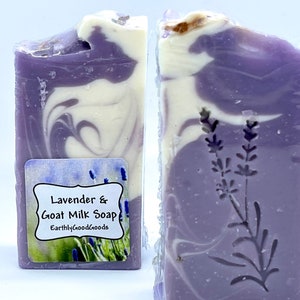 K&ouml;nnte beinhalten: Eine Seife mit Lavendel und Ziegenmilch mit einem Wirbelmuster in Violett- und Wei&szlig;t&ouml;nen. Die Seife hat ein Etikett mit der Aufschrift "Lavender & Goat Milk Soap" und "EarthlyGoodGoods".