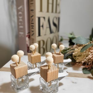 May include: Four clear glass bottles with wooden tops and wooden sticks with white balls on the ends. The bottles are sitting on a white surface.