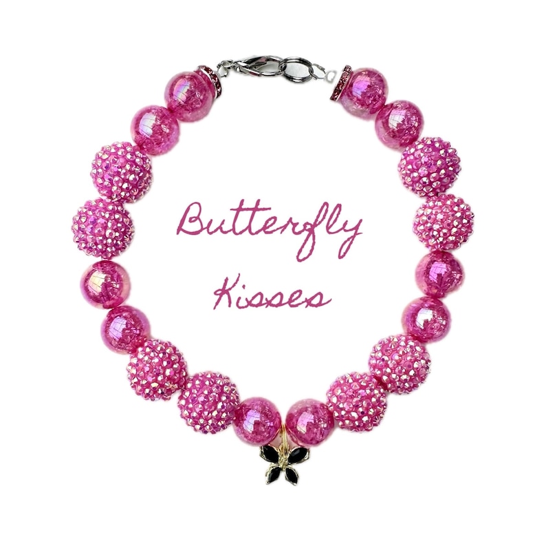 K&ouml;nnte beinhalten: Rosa Perlenarmband mit einem Schmetterlingsanh&auml;nger. Die Perlen sind irisierend und haben eine glitzernde Oberfl&auml;che. Das Armband hat einen silbernen Verschluss und der Text "Butterfly Kisses" steht in der Mitte.