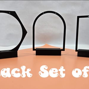 May include: A set of three black display frames in geometric shapes: a hexagon, an arch, and a square. Each frame is mounted on a rectangular base. The text "Black Set of 3" is displayed in white, bubbly letters.