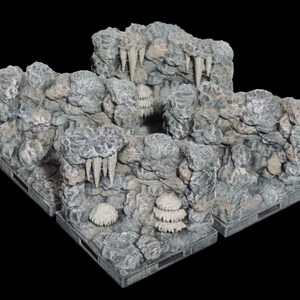 Puede incluir: Tres formaciones rocosas grises y blancas texturizadas con detalles en forma de estalactitas y una abertura de cueva. Las formaciones están sobre un fondo negro.