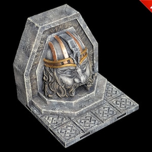 Puede incluir: Una escultura de piedra gris de una cara con un casco dorado y marrón. La escultura está integrada en una pared de piedra con una base de piedra decorativa.