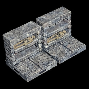 Puede incluir: Dos secciones de pared de piedra en miniatura con estantes, cada una con un esqueleto. Las paredes son de piedra gris con una textura rugosa y están colocadas sobre una base de baldosas de piedra gris.