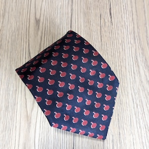 以下が含まれることがあります： 赤いチェリーが繰り返し描かれた、濃い青色のシルクネクタイです。