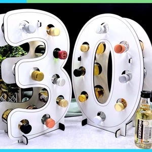 May include: White wooden wine rack in the shape of the numbers 3 and 0, holding several small bottles of wine. The rack is designed to hold multiple bottles, with a variety of colorful bottle caps visible. A small bottle of ginger liqueur is next to the rack.
