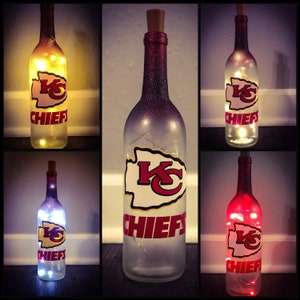 May include: Six wine bottles with a Kansas City Chiefs logo and lights inside. The bottles are decorated with a red, white, and gold color scheme. The bottles are lit with white, yellow, and red lights.