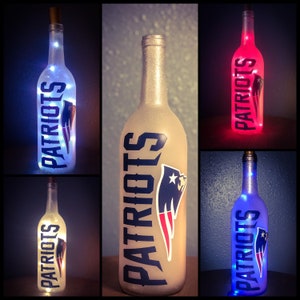 May include: Three wine bottles with lights inside, each with a different color light: blue, white, and red. Each bottle has a Patriots logo and the word "Patriots" written on it.