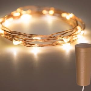 May include: Copper wire string lights with warm white LED bulbs. The lights are wrapped around a cork bottle stopper with a switch.