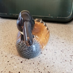 May include: A wooden carved duck decoy with a black head and a brown and white body. The duck is lying on its side with its head turned to the side.