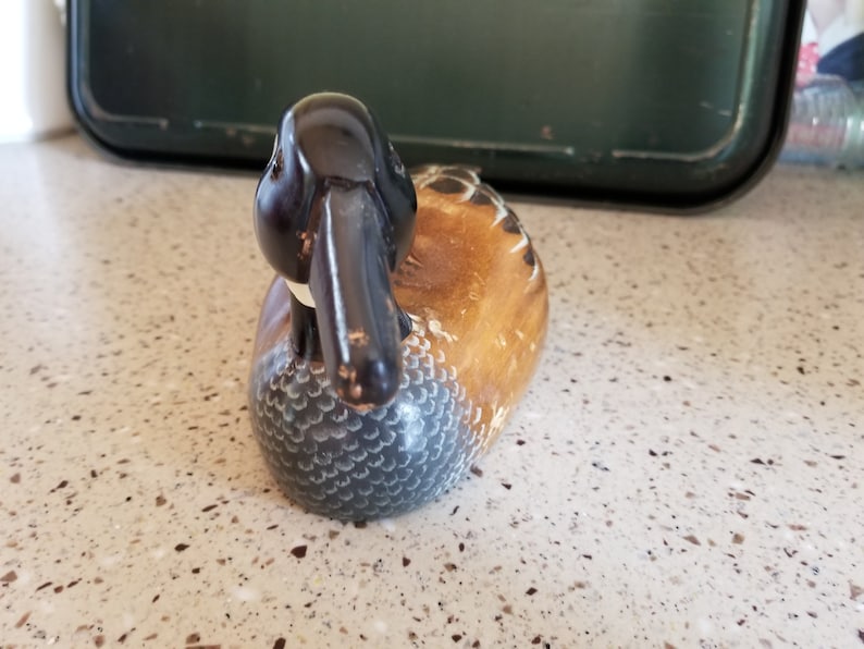 May include: A wooden carved duck decoy with a black head and a brown and white body. The duck is lying on its side with its head turned to the side.