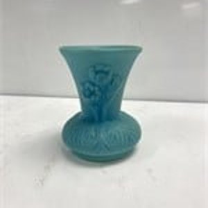 Puede incluir: Un pequeño jarrón de vidrio azul claro con un diseño floral. El jarrón tiene una parte superior acampanada y una base redondeada.