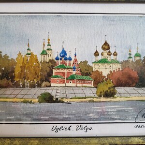 May include: A watercolor painting of a cityscape with a river in the foreground. The city is dominated by a cluster of colorful churches with onion domes. The painting is signed and dated "1935" in the lower right corner. The text "Uglitch. Volga." is written in the lower center of the painting.