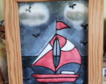 May include: A framed stained glass artwork depicting a red sailboat with white and black accents sailing on a dark blue sea with white clouds in the background.