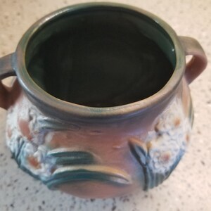 May include: A brown ceramic pot with two handles and a green glaze. The pot is decorated with white flowers and green leaves.