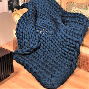 May include: A large, chunky knit throw blanket in a deep blue color. The blanket is draped over a couch and has a thick, textured weave.