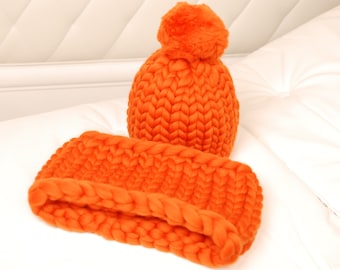 May include: A bright orange knitted hat and matching headband. The hat has a fluffy pom pom on top.