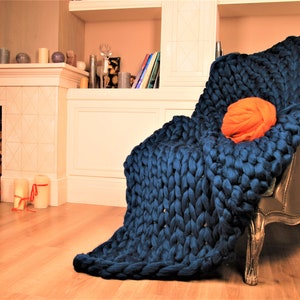 May include: A large, chunky knit throw blanket in a deep blue color draped over a chair. The blanket is made of thick yarn and has a soft, cozy texture.