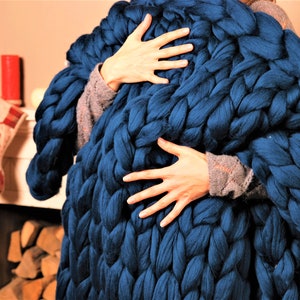 May include: A large, chunky knit blanket in a deep blue color. The blanket is made of thick yarn and has a soft, cozy texture.