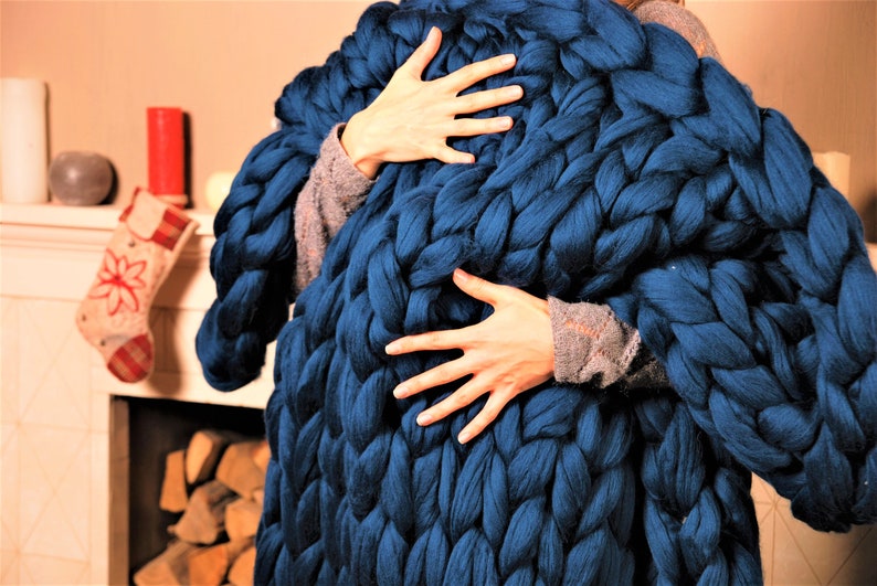 May include: A large, chunky knit blanket in a deep blue color. The blanket is made of thick yarn and has a soft, cozy texture.