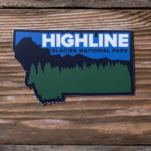 May include: A rectangular sticker in the shape of Montana, featuring the text "HIGHLINE GLACIER NATIONAL PARK" in white and blue. The design includes a dark blue mountain range, green trees, and a blue sky background.
