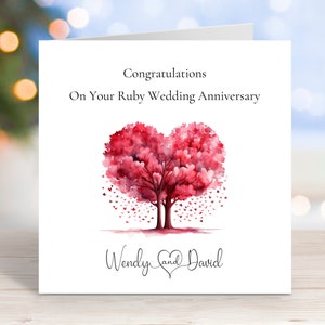 May include: A greeting card featuring a watercolour illustration of two trees forming a heart shape. The trees are red and have small pink hearts for leaves. The text "Congratulations on Your Ruby Wedding Anniversary Wendy and David" is printed on the card.