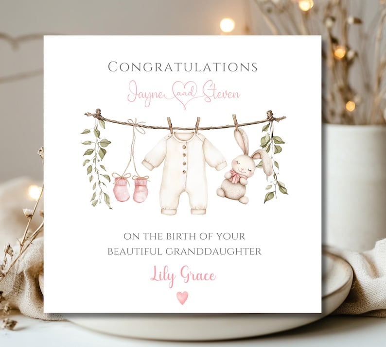 May include: A square greeting card with the words "Congratulations" and "On the birth of your beautiful granddaughter". The card features a watercolour illustration of baby clothes, a bunny, and the names "Jayne and Steven" and "Lily Grace".