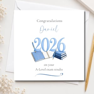 May include: A square greeting card with a white background featuring the text Congratulations Daniel 2026 on your A-Level exam results. The design includes a watercolour illustration of blue notebooks, stacked books, and two blue pens.