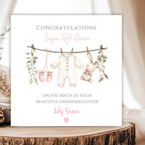 May include: A baby announcement card with the words "Congratulations" and "On the birth of your beautiful granddaughter". The card features a watercolour illustration of baby clothes, a bunny, and greenery hanging on a washing line. The baby's name is "Lily Grace".