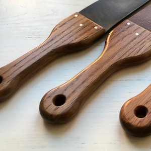 Puede incluir: Tres herramientas de trabajo del cuero con mango de madera y diferentes materiales de hoja. Las hojas están hechas de cuero, metal y madera. Los mangos están hechos de madera oscura con detalles en latón.