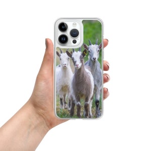 May include: A phone case featuring a photograph of three goats in a field. The goats are white, grey, and brown. The case is clear with a white border.