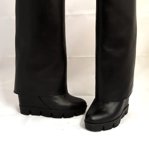 Peut inclure: Une paire de bottes en cuir noir &agrave; talon compens&eacute;. Les bottes ont un revers rabattable en haut.