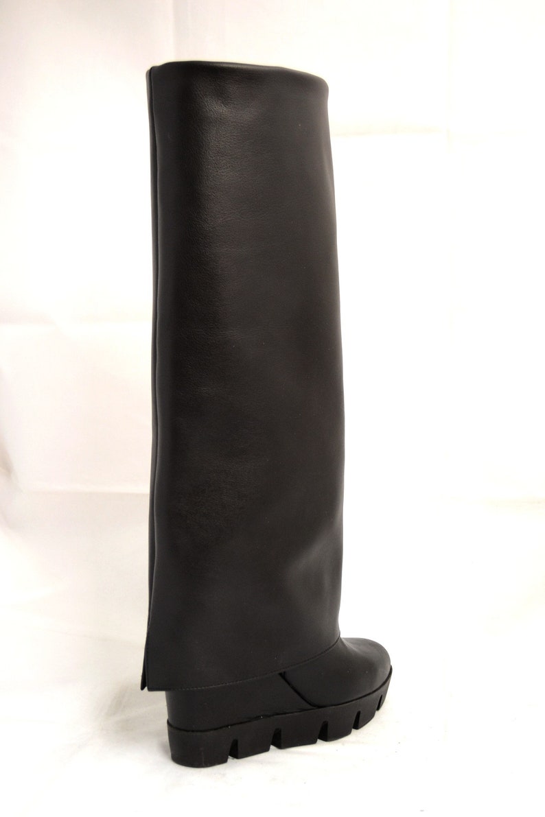 Peut inclure: Bottines noires en cuir montant au genou avec une &eacute;paisse semelle plateforme et un revers pli&eacute;.