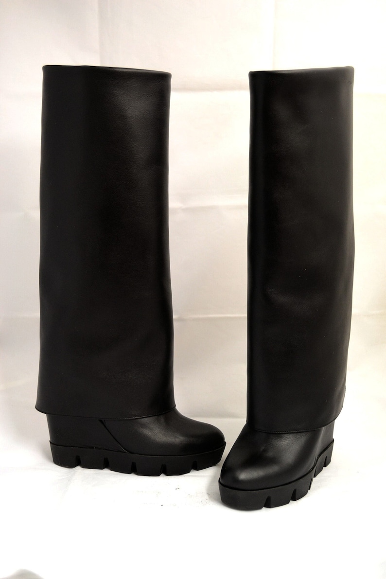 Peut inclure: Une paire de bottes en cuir noir &agrave; talon compens&eacute;. Les bottes ont un revers rabattable en haut.