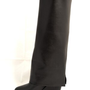 Peut inclure: Bottines noires en cuir montant au genou avec un talon compens&eacute; et un revers.