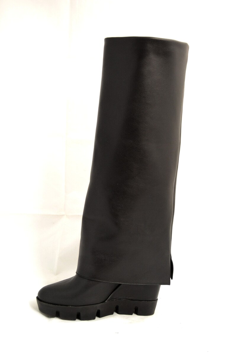 Peut inclure: Bottines noires en cuir montant au genou avec un talon compens&eacute; et un revers.
