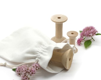 May include: Three wooden spools of different sizes, one inside a white cotton drawstring bag, with pink flowers on a white background.