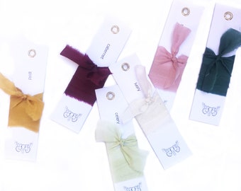 May include: Six fabric swatches on white cards with labels: Gold, Cabernet, Ivory, Celery, and two unlabeled swatches. The swatches are tied with bows and are arranged on a white surface.