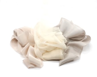 May include: Three pieces of silk ribbon in shades of beige, cream, and light brown. The ribbon is arranged in a loose pile.