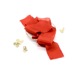 May include: A red silk ribbon is draped over a small white plate. The ribbon is soft and flowing, and the color is a rich, vibrant red. The plate is simple and elegant, and the ribbon is a beautiful contrast to the white.