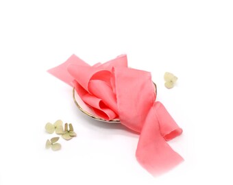 May include: A pink silk ribbon is arranged on a white plate with a gold rim. The ribbon is soft and flowing, and the color is a delicate shade of pink.
