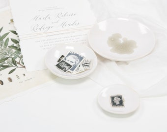 May include: Three white ceramic dishes with gold rims. The largest dish is empty. The medium dish contains several vintage postage stamps. The smallest dish contains a single vintage postage stamp.