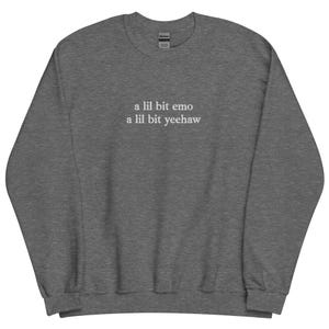May include: Charcoal grey sweatshirt featuring the white text "a lil bit emo a lil bit yeehaw". The sweatshirt has a crew neck and long sleeves. The Gildan brand label is visible at the back of the neck.